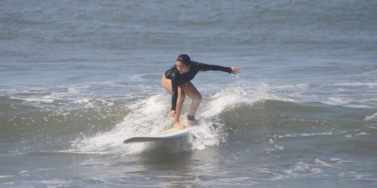 A student crouched and balanced on a white board as the wave carries her towards shore
