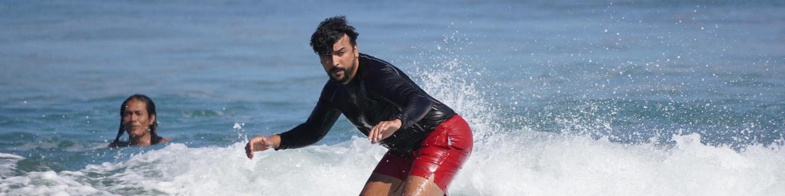 A surfer riding across the face of a clean wave while another paddles out behind him